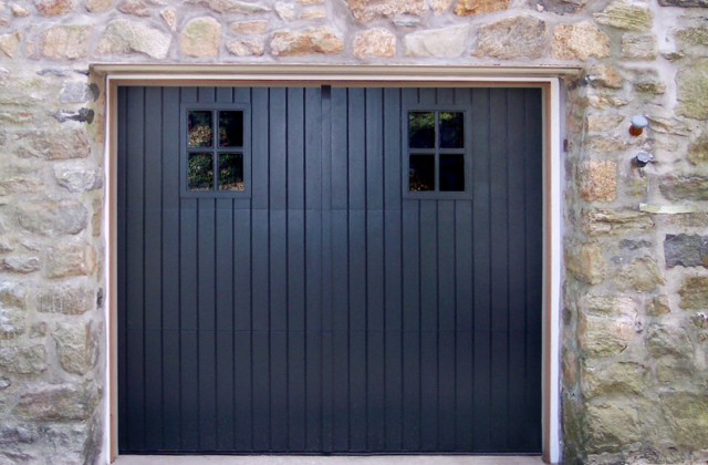 Black barn styled garage door with garage door windows on a stone garage