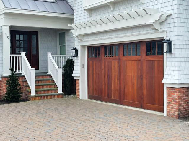 Four paneled real wood garage door installed on a white beach house with a stone driveway