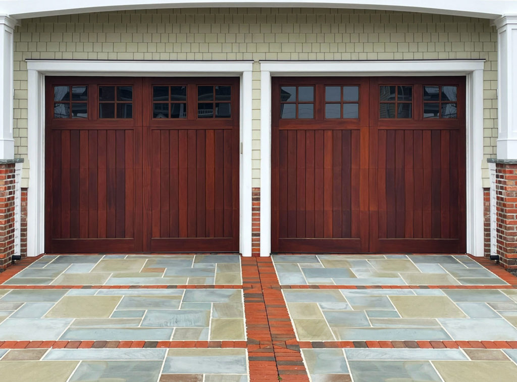 Dark stained real wood garage door at the end of a flagstone and brick driveway
