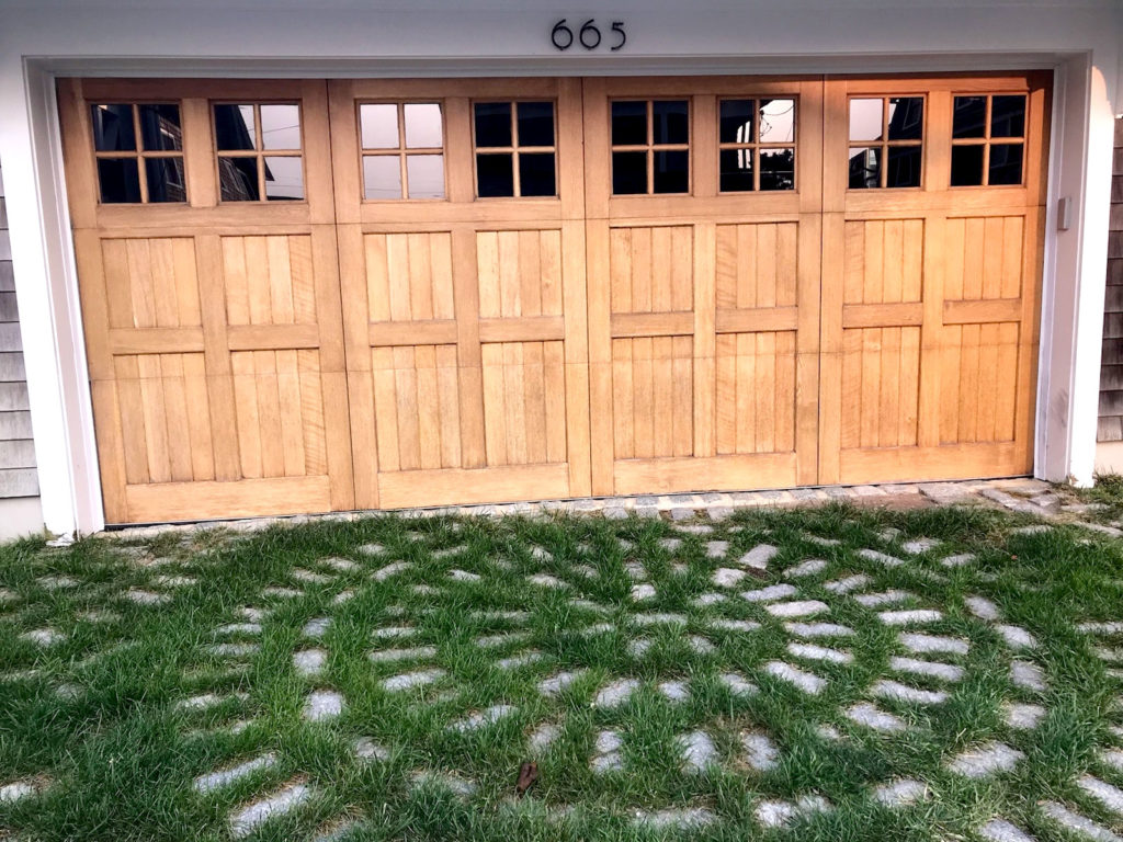 Light real wood garage door in front of a geometric grass driveway