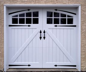 White vinyl garage door with two arched windows, strap hinges, and door handles on a beige garage