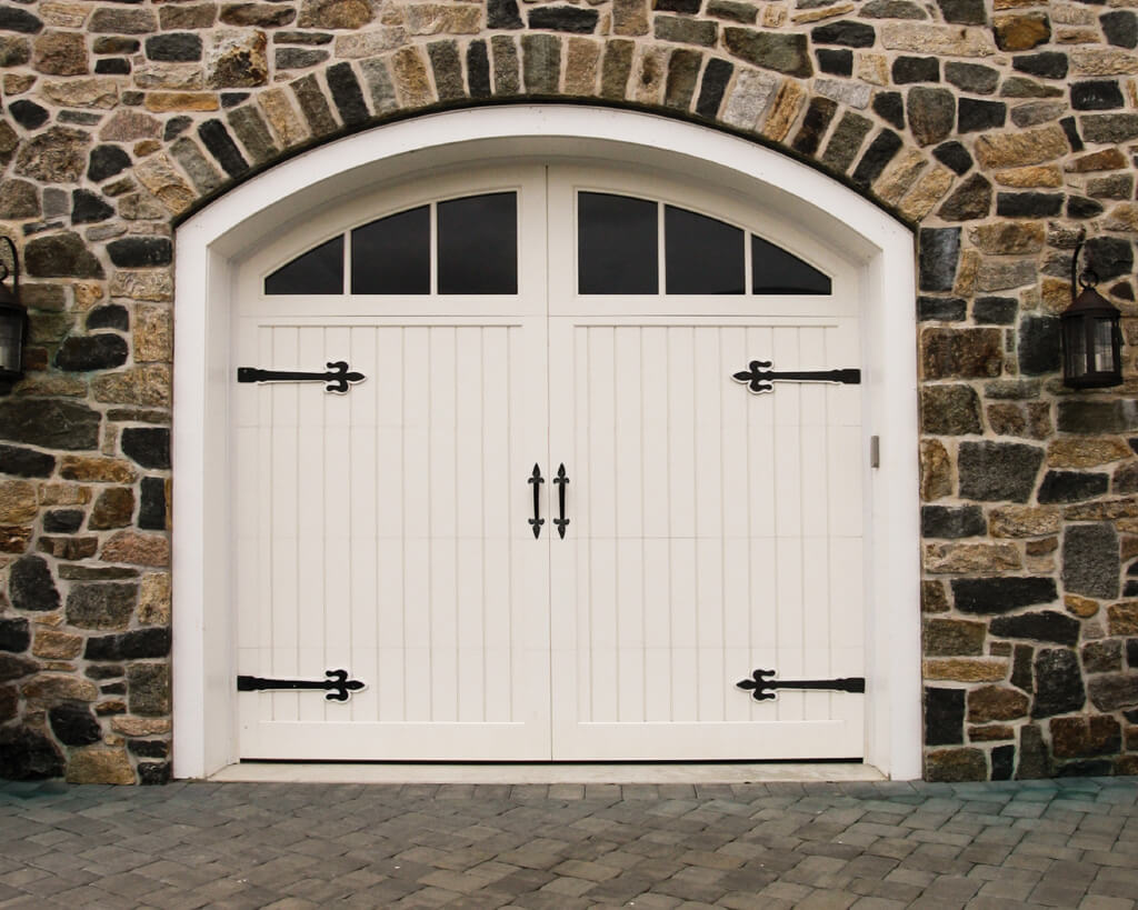 White vinyl Symphony garage with decorative garage door hardware and windows on stone garage