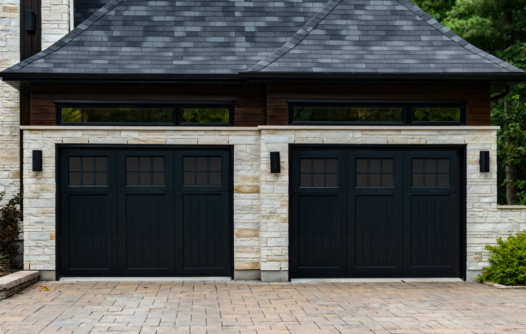 Stained black accoya wood garage door with tri fold panel on a stone garage