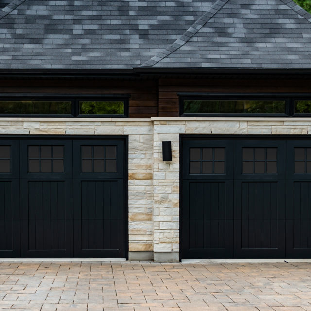Stained black accoya wood garage door with tri fold panel on a stone garage