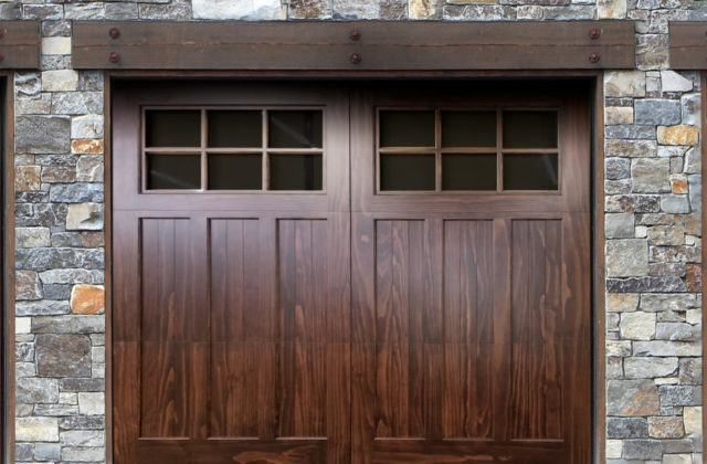 Brown accoya wood garage door with three planels, windows on a natural stone garage