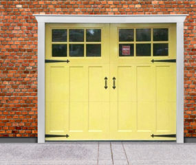 Yellow wood composite garage door with square windows, strap hinges, and door handles on brick garage