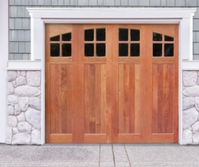 Natural brown wooden garage door with four windows on gray wood and stone garage
