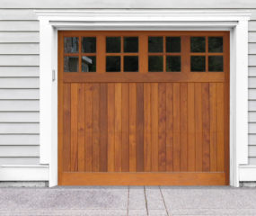 Brown wooden garage door with four windows on gray vinyl garage