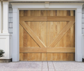 Natural brown wood swing out garage door with v bucks on gray wood garage