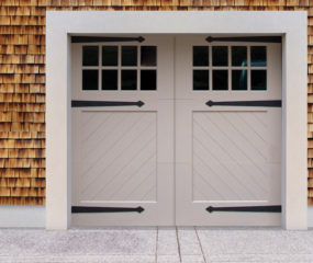 Light gray swing out garage door with two windows, and door straps on brown wood garage