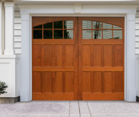 Brown stained wooden swing out carriage garage door with two windows and low cross rail