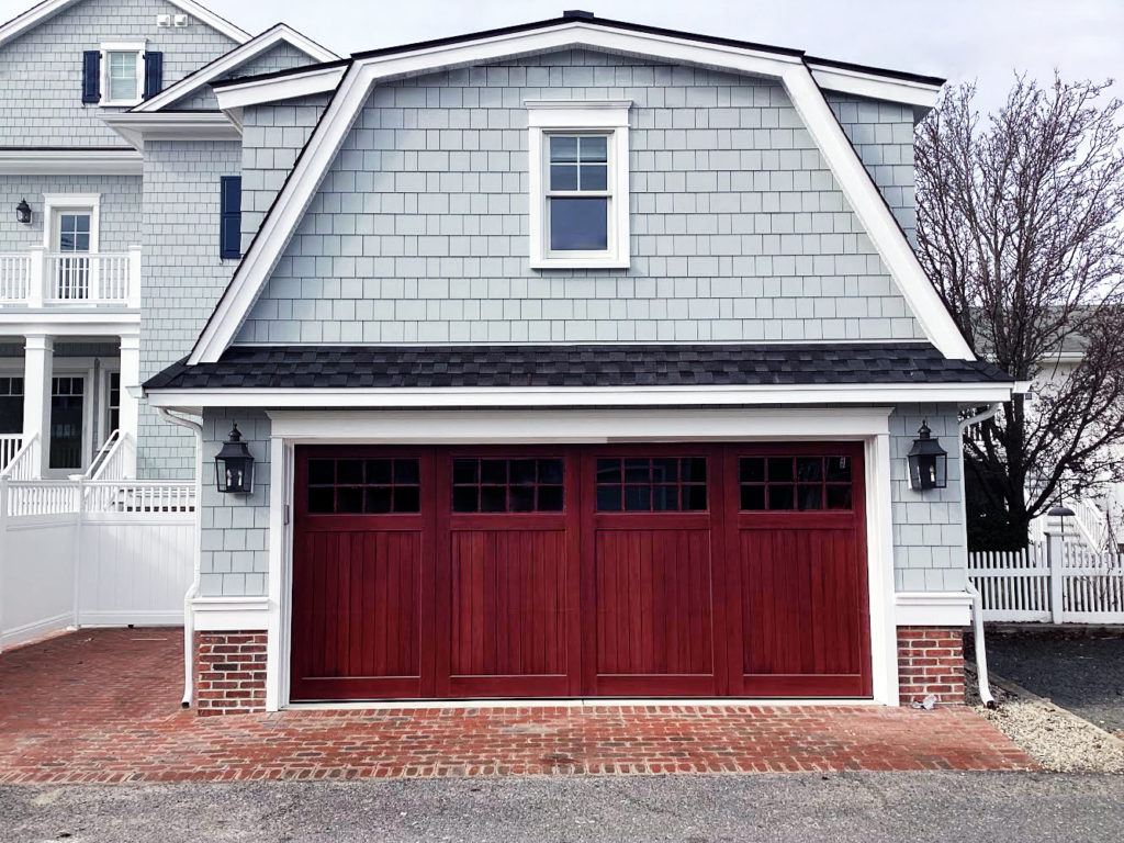 Red stained accoya wood garage door with windows on a vinyl gray garage