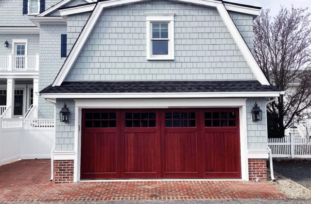Red stained accoya wood garage door with windows on a vinyl gray garage