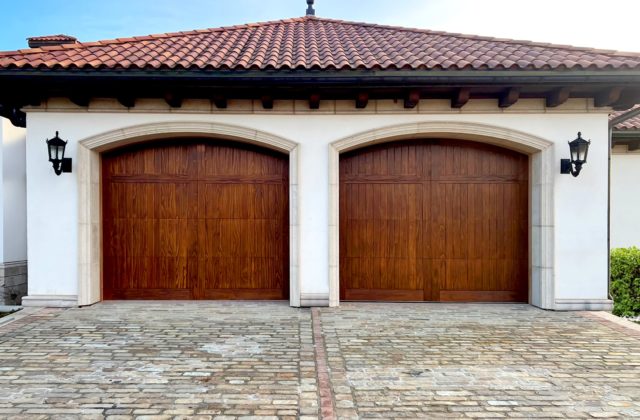wooden double garage door with exterior lighting lamps on either side.