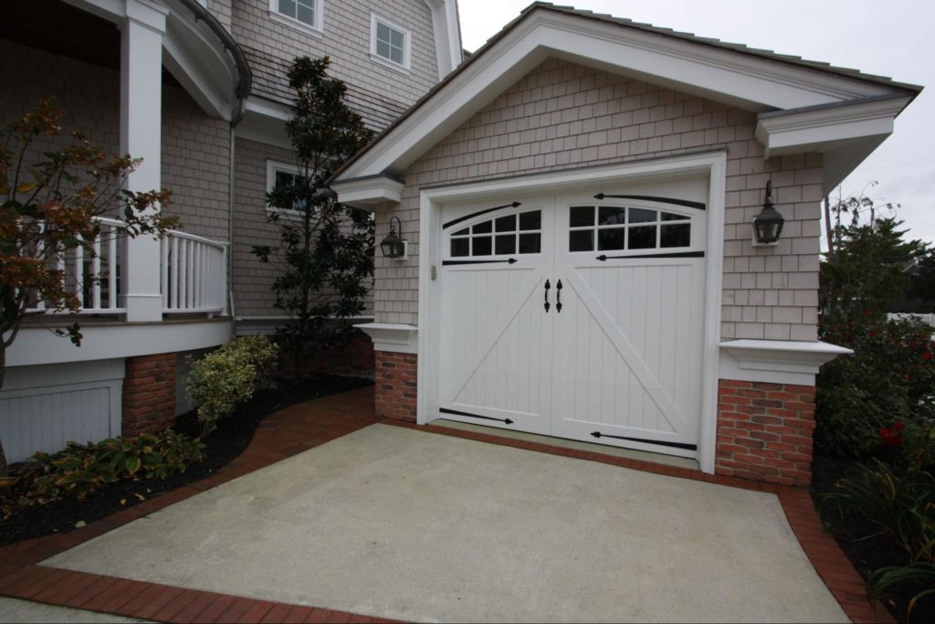 A detached shed with a white garage door with decorated hardware and windows. 