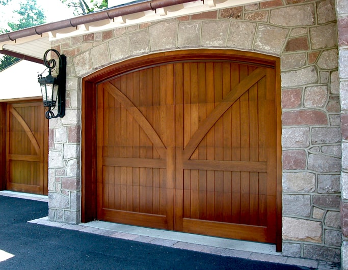 A stone siding and light wood garage door with a lantern to the left of the garage door.