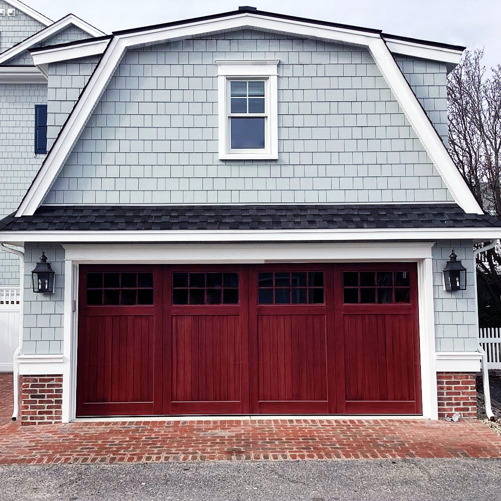 Red stained accoya wood garage door with windows on a vinyl gray garage