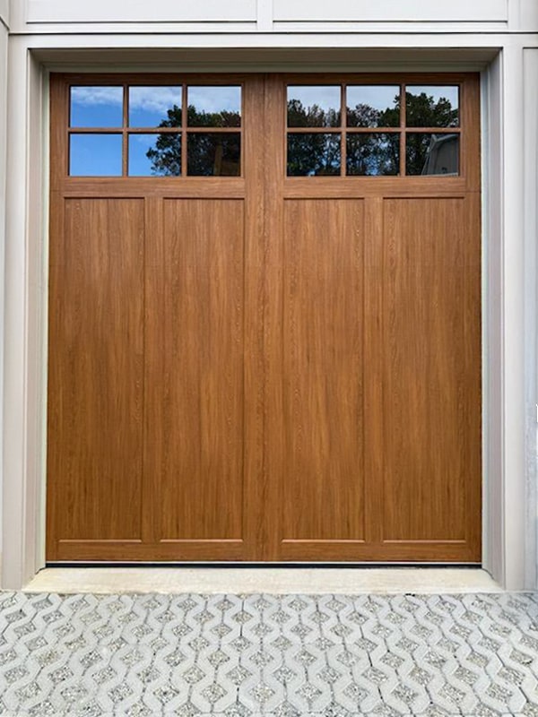 composite wood garage door with a warm wood finish and top window inserts.