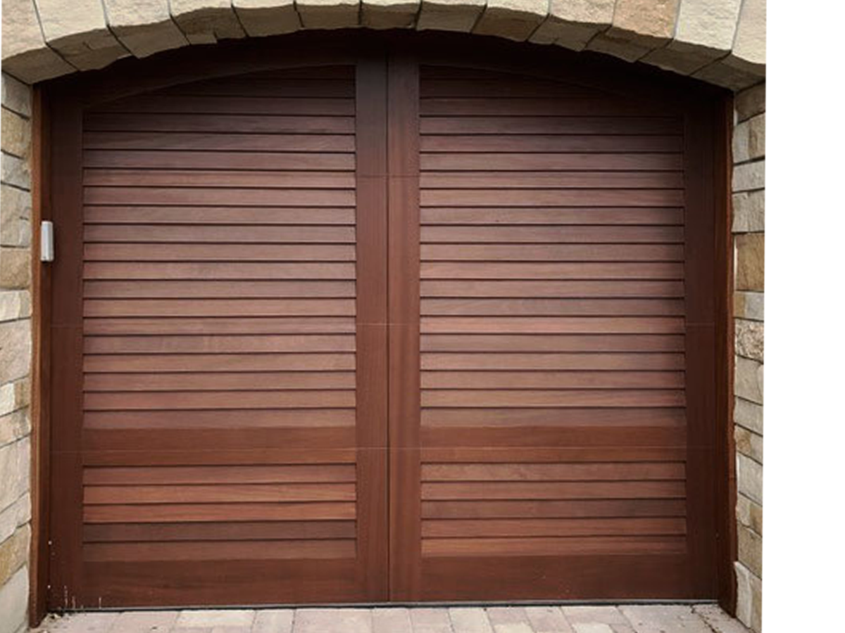 Brown swing out wooden arched garage door with no windows on stone garage