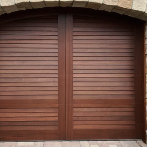 Brown swing out wooden arched garage door with no windows on stone garage