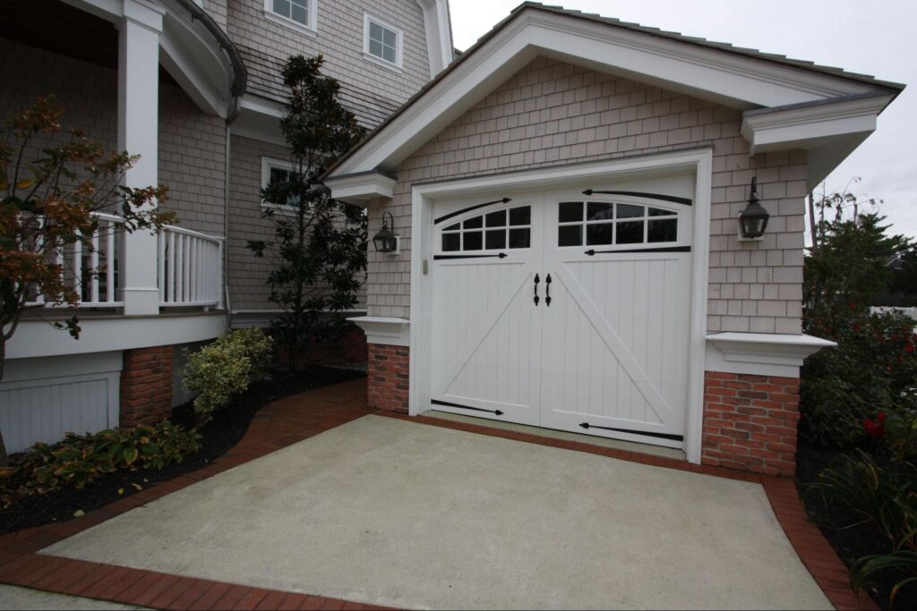 A detached shed with a white garage door with decorated hardware and windows.