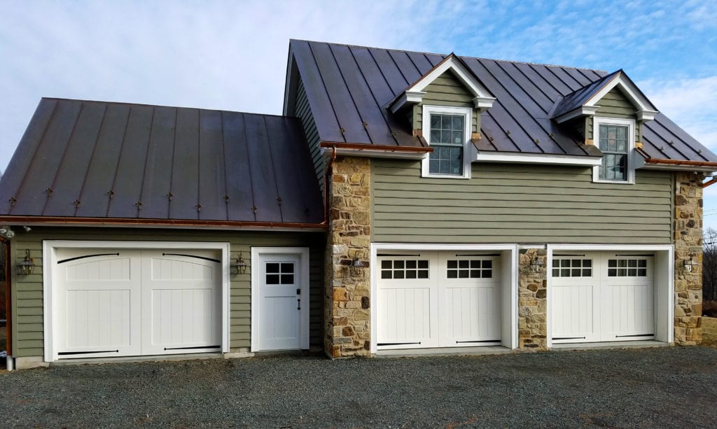 A green detached garage space with three white garage doors.