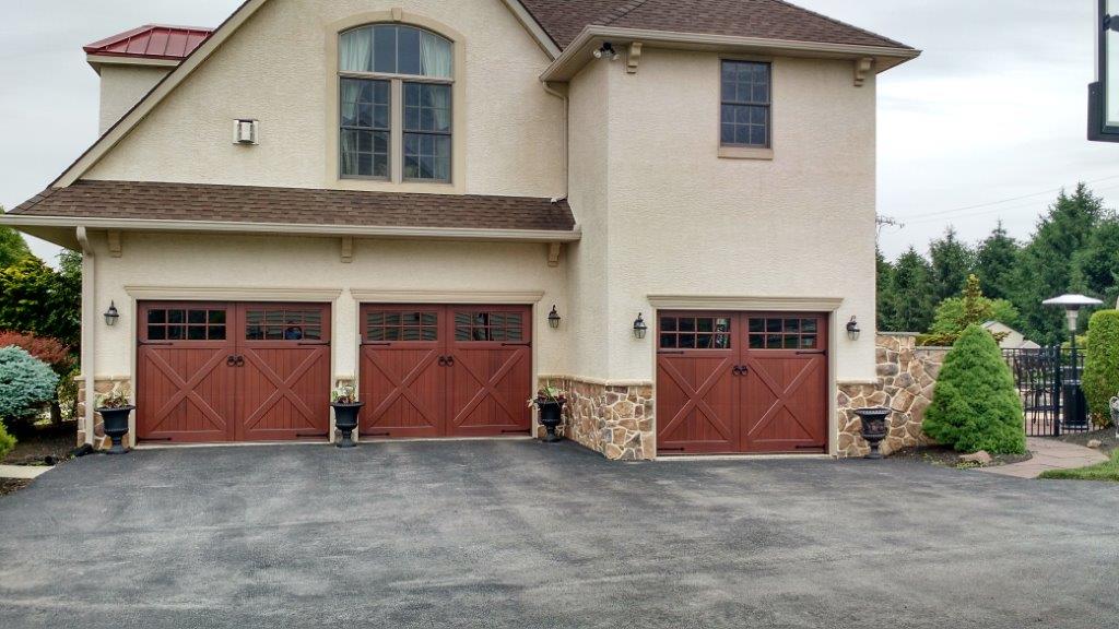 The side of the house shows three red garage doors with windows and ring pulls.